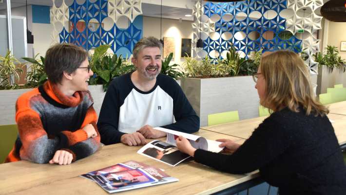 3 mensen in gesprek. Een foto met daarop de handleiding Leef je eigen leven, onderdeel van het project Capability College, Volwaardig Leven met Autisme