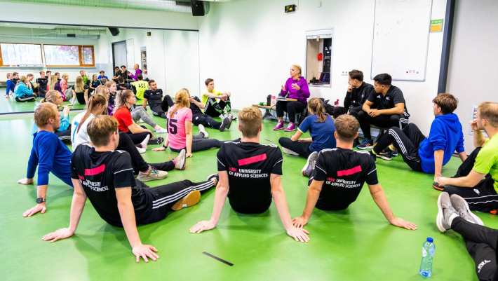 Studenten luisteren in de sportles naar docente.