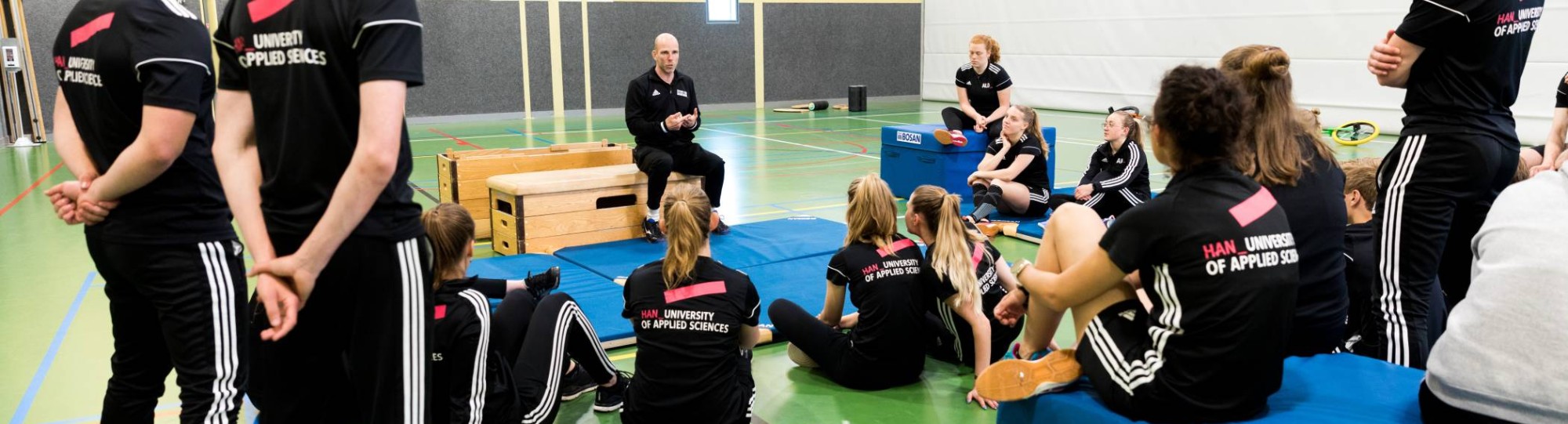 Pabo-ALO studenten zitten in de gymzaal rondom de docent die instructies geeft.