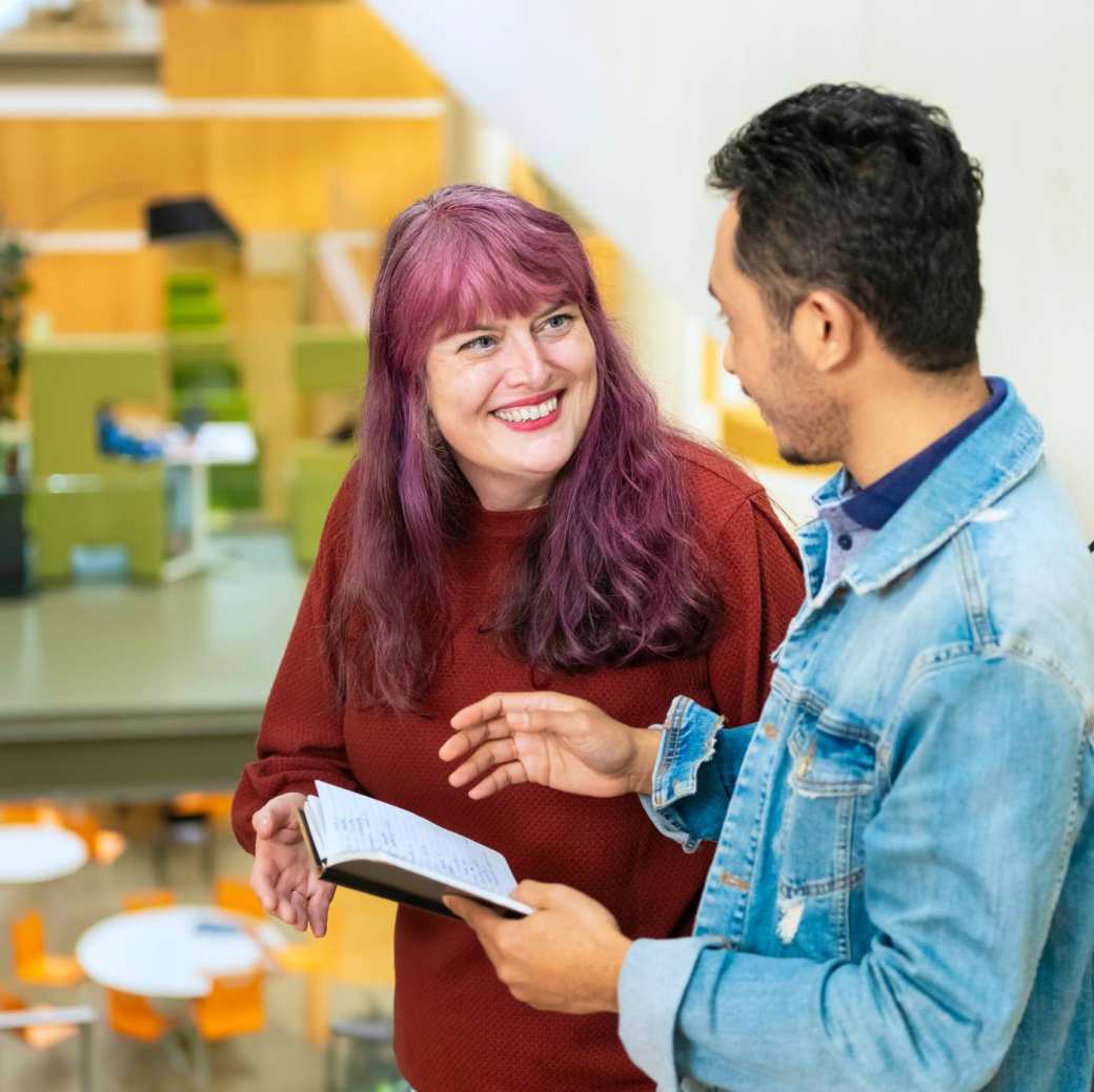 Twee studenten vertellen met elkaar terwijl de een een kladje in de hand heeft met geschreven tekst.
