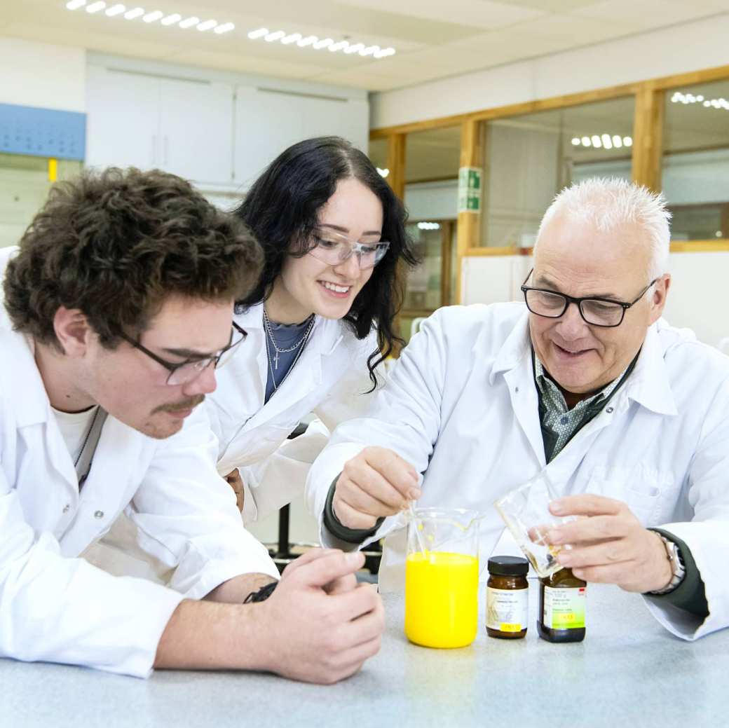 Twee studenten voeren met docent een proef uit in het lab