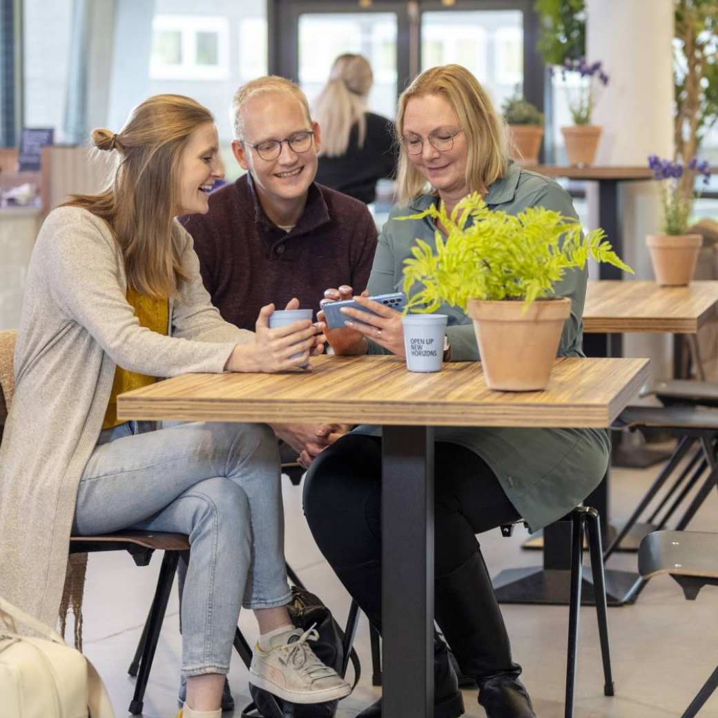 3 Studenten aan de koffie in een café. Kijken lachend naar iets op een mobiel.