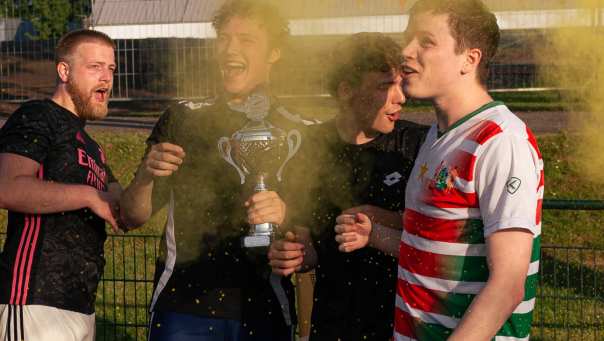 4 guys celebrating. the second one from the left is holding a trophy. yellow confetti.