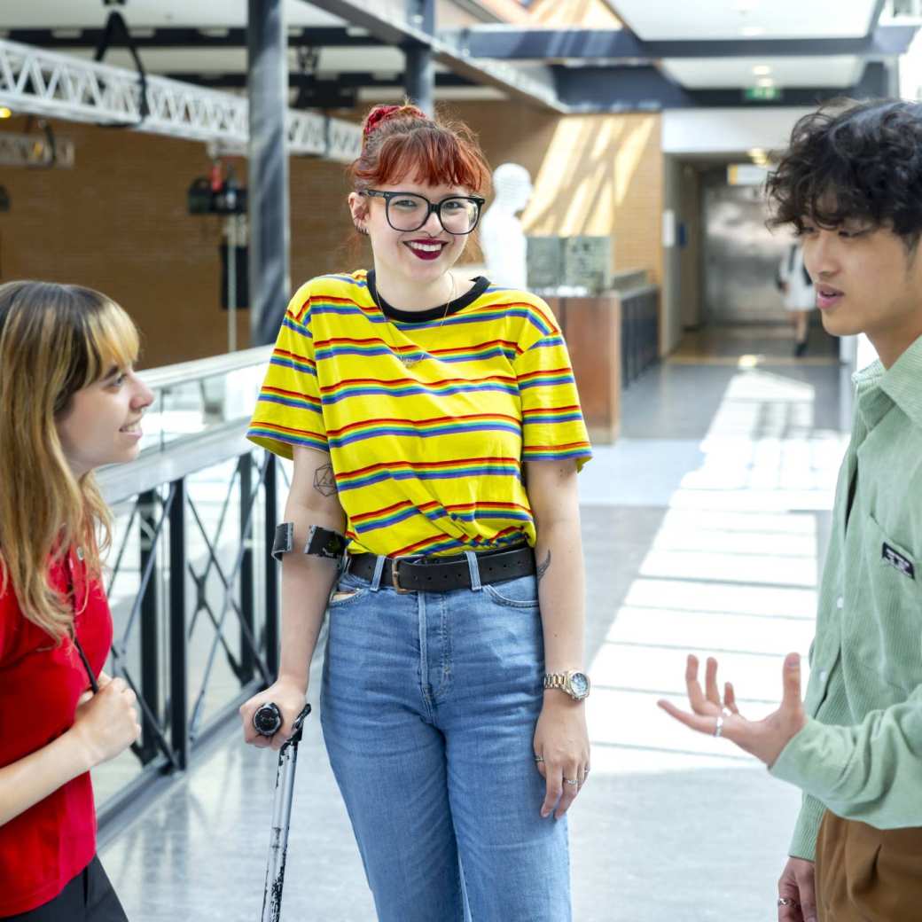 Drie studenten staan met elkaar te praten. Loopbrug K33. Student met bijzondere omstandigheden kijkt in lens. Fotoshoot 2023.