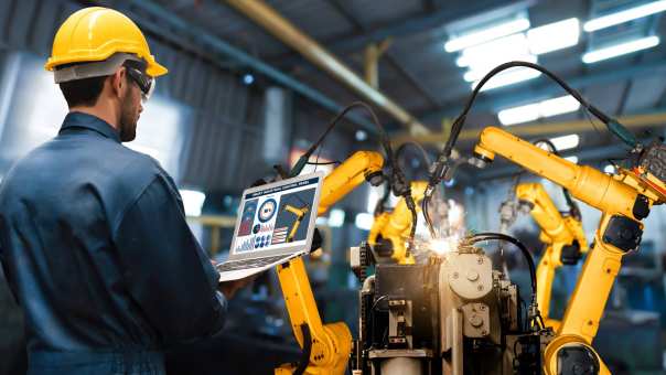 Man met tablet kijkt naar robotarmen in Digitale Fabriek