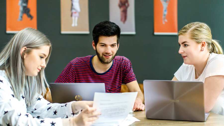 Twee studenten kijken naar wat hun medestudent aanwijst op het A4'tje. 