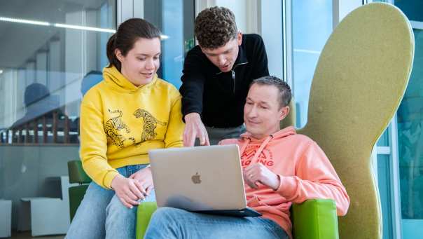 Drie studenten in de masters economie overleggen bij een laptop.