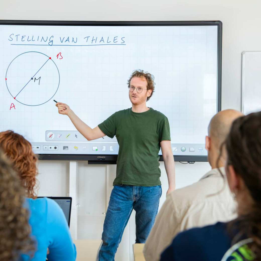 Twee studenten werken samen achter de laptop in het I/O gebouw en kijken lachend naar het scherm.