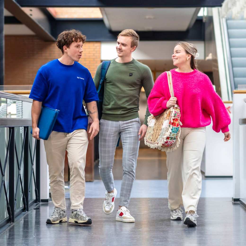 3 studenten lopen op de gang, richting de camera.