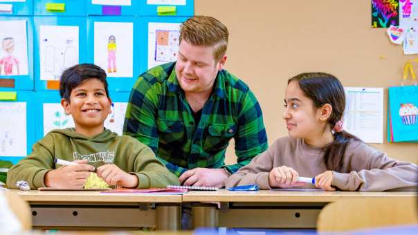 Meester kijkt mee bij kinderen in de klas