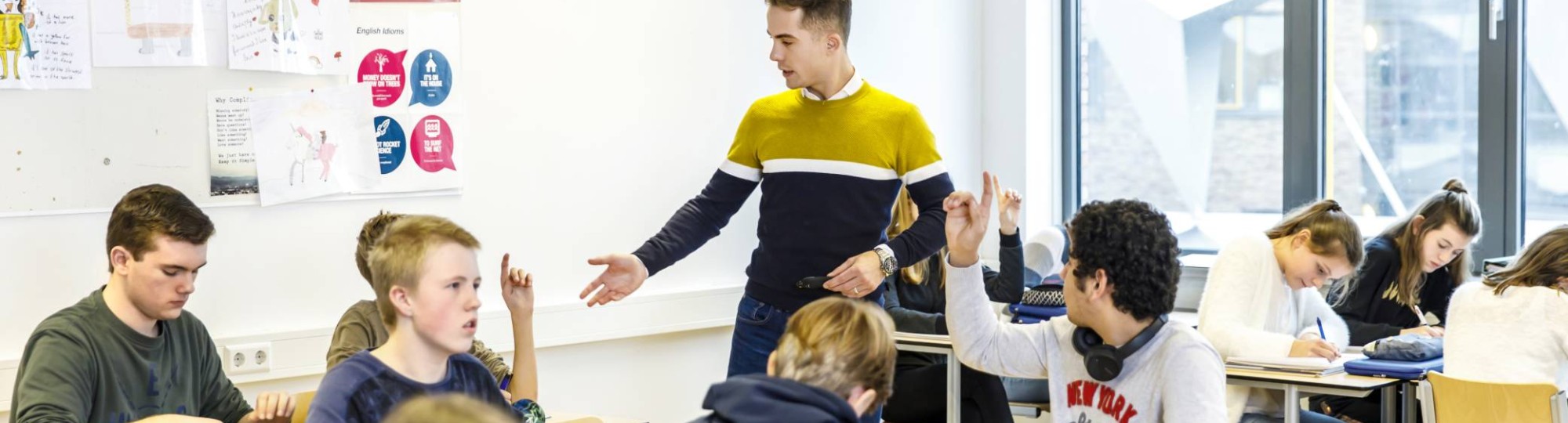 Docent op het Citadel College loopt door het klaslokaal om vragen van de leerlingen te beantwoorden die de vinger in de lucht hebben.