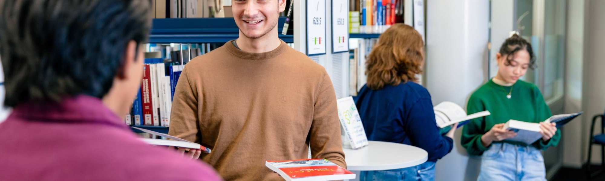 International students Diego, Andrei, Noa and Tam browsing through books in the library on the Arnhem campus of HAN University of Applied Sciences.