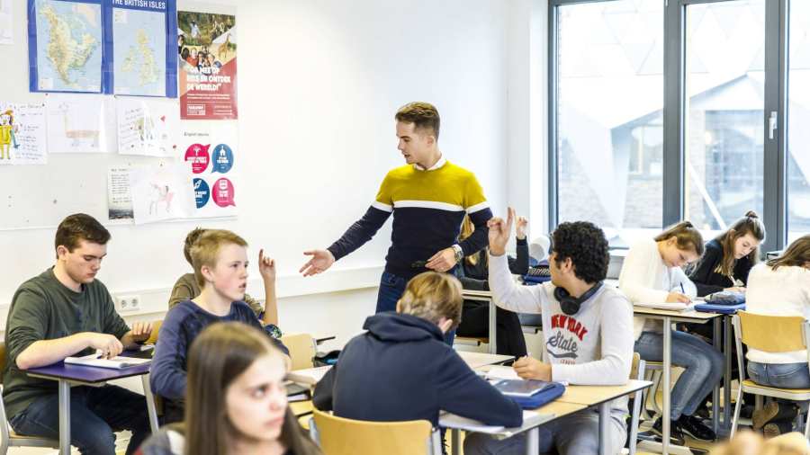 Docent op het Citadel College loopt door het klaslokaal om vragen van de leerlingen te beantwoorden die de vinger in de lucht hebben.