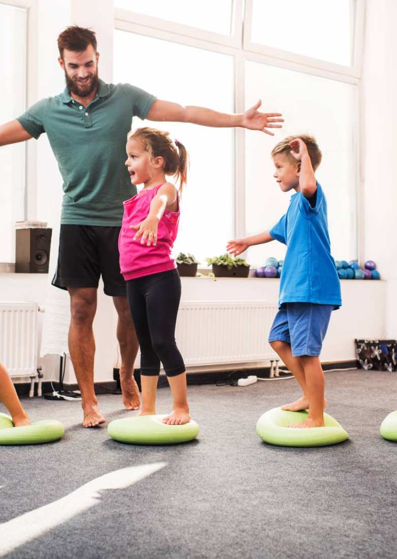 kinderen wandelen op pilates-ballen tijdens training op sportschool met mannelijke coach