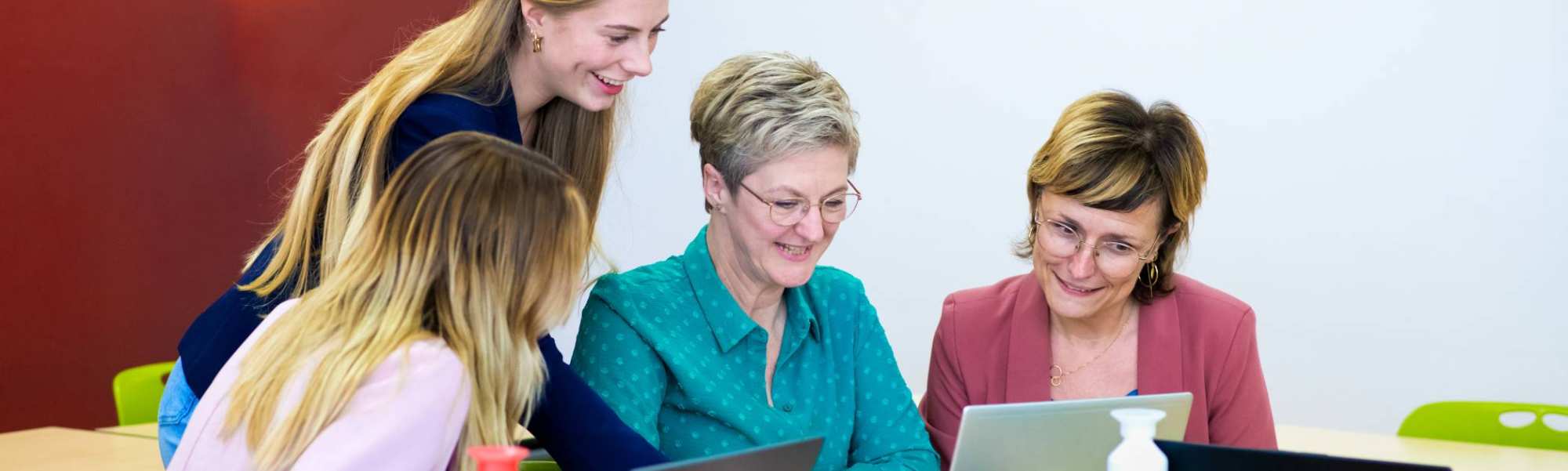 Vier studenten kijken samen op één scherm, terwijl iedereen een laptop heeft.