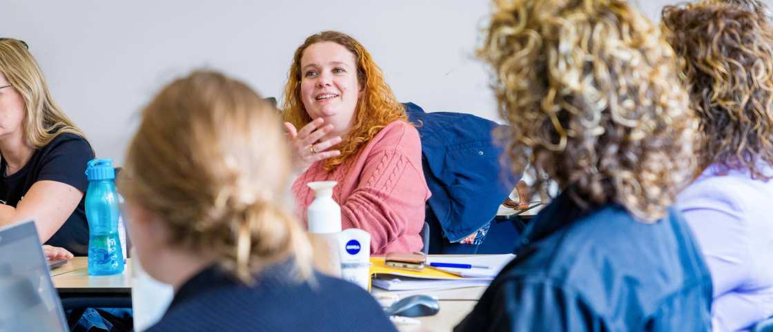 Vrouw in roze trui is in gesprek met docent tijdens de cursus acute pijn service.