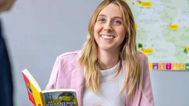 Student heeft een boek in haar hand en lacht.