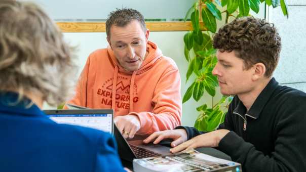 2 masterstudenten zitten samen terwijl één van hen uitleg geeft en wat aanwijst op het laptopscherm