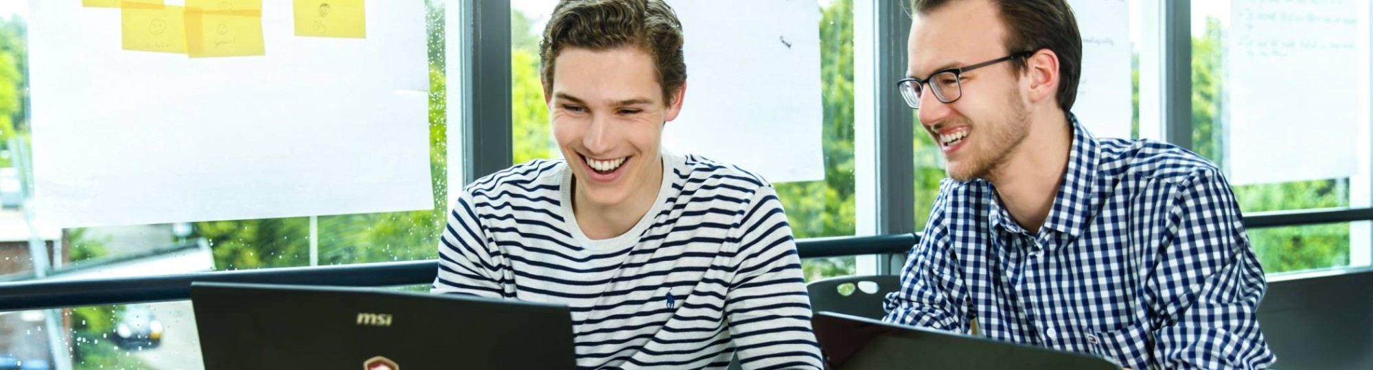 2 deeltijdstudent achter hun laptops lachen.