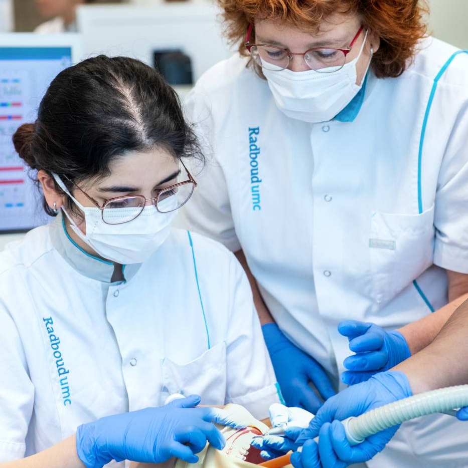 student oefent op pop en docent kijkt mee