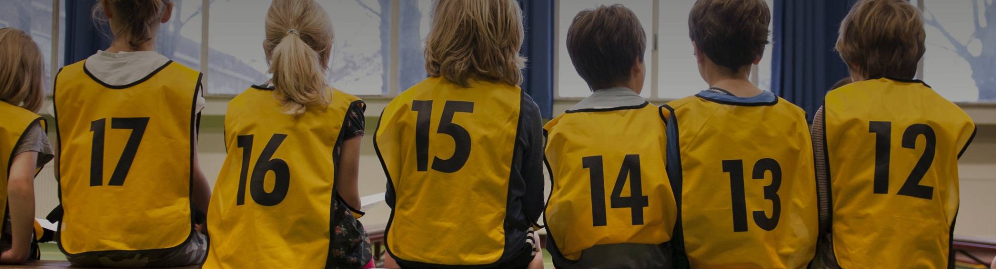 Kinderen in een gymzaal met hesjes aan op de rug gefotografeerd