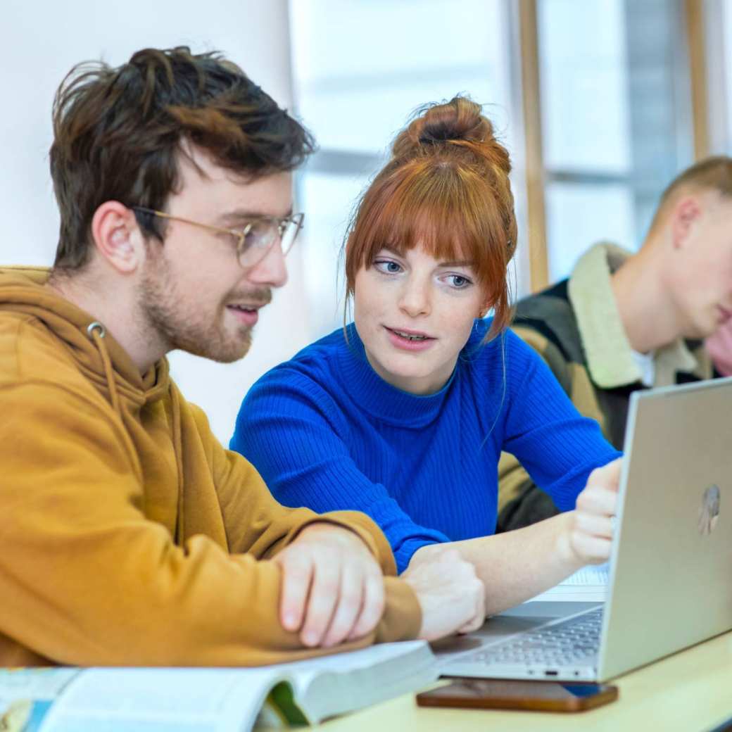 Twee studenten zitten in de mediatheek en kijken geconcentreerd naar de laptop.