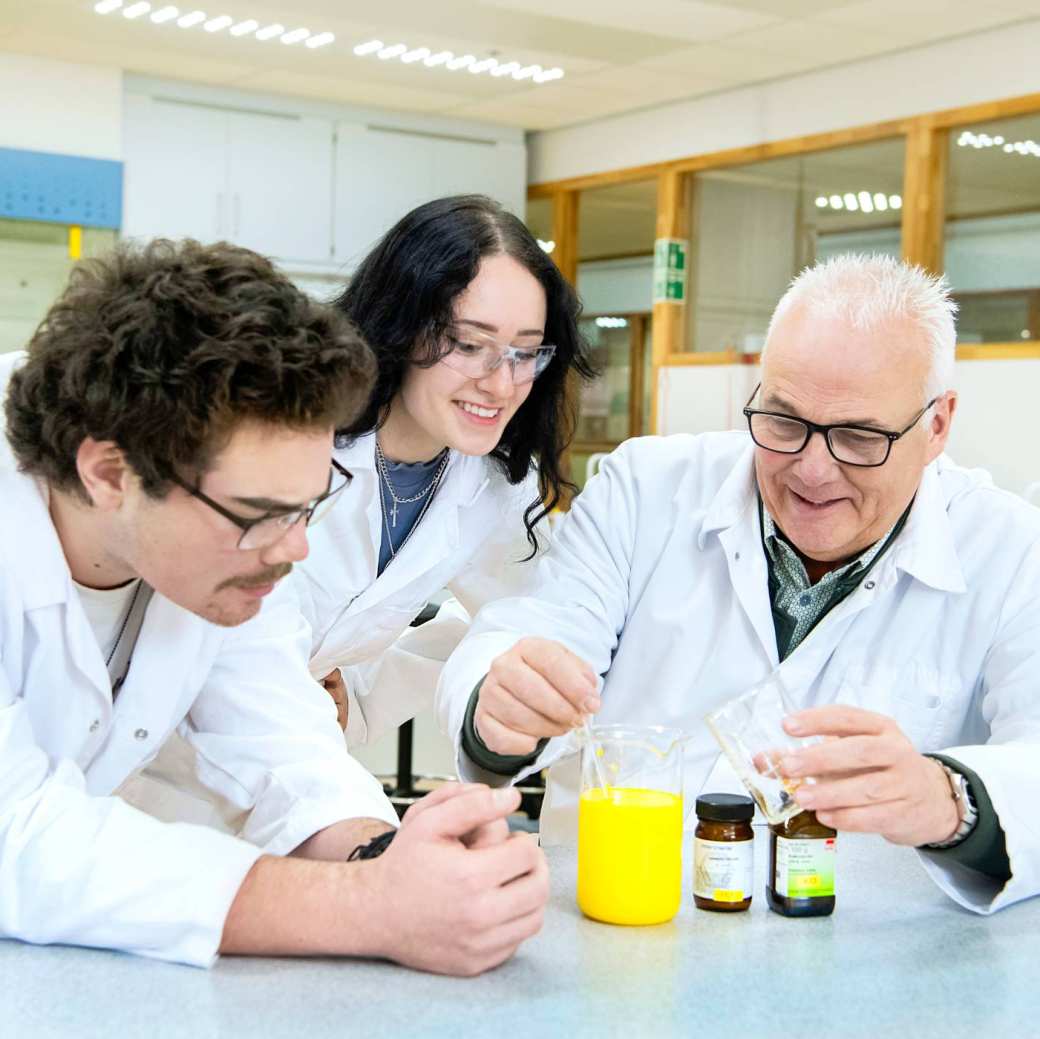 Twee studenten doen scheikundeproef in opleiding tot leraar met een docent.