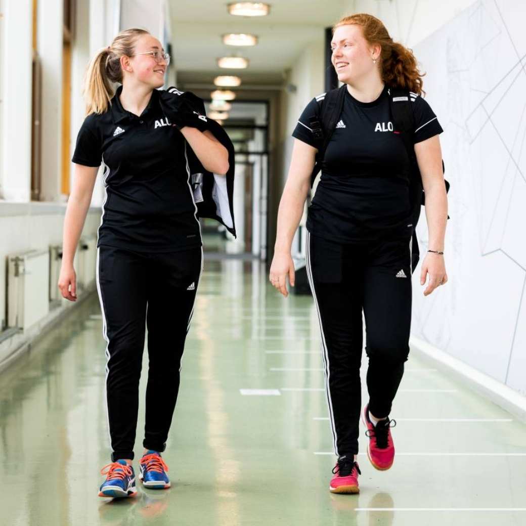 Twee vrouwelijke studenten van de Pabo-ALO lopen in de gang in hun zwarte ALO-tenue.