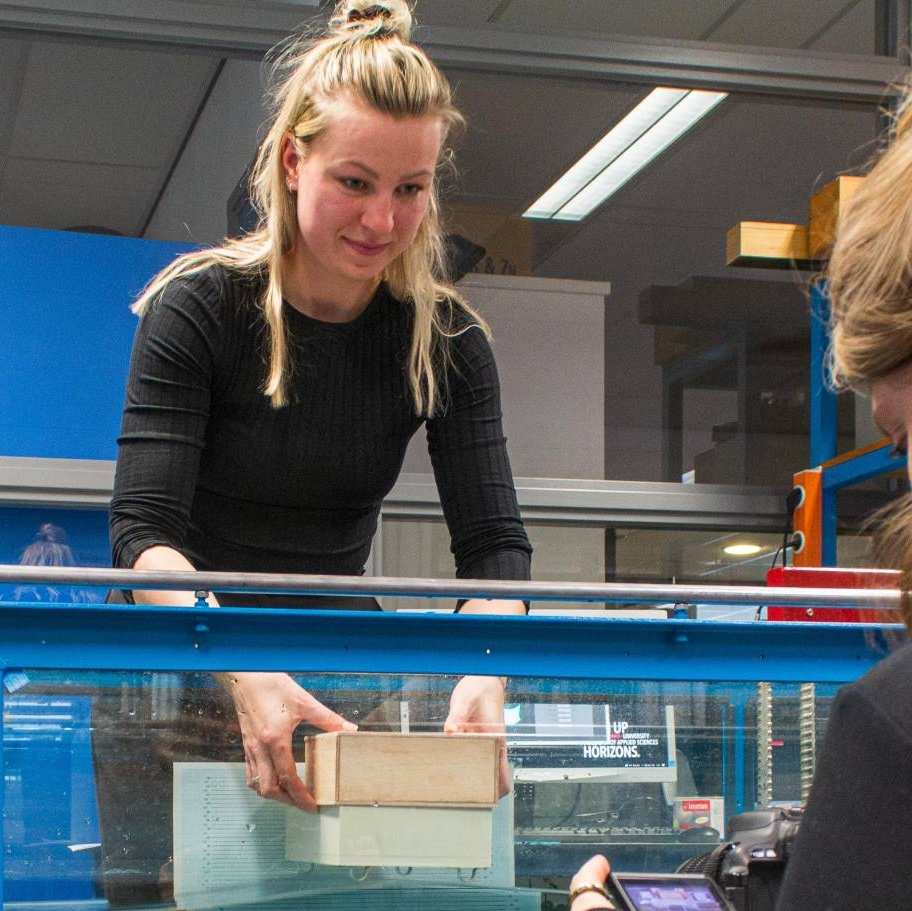 Nienke Maas en Brechtje Kraaijvanger doen een proef in het waterlab met het model van een woonboot