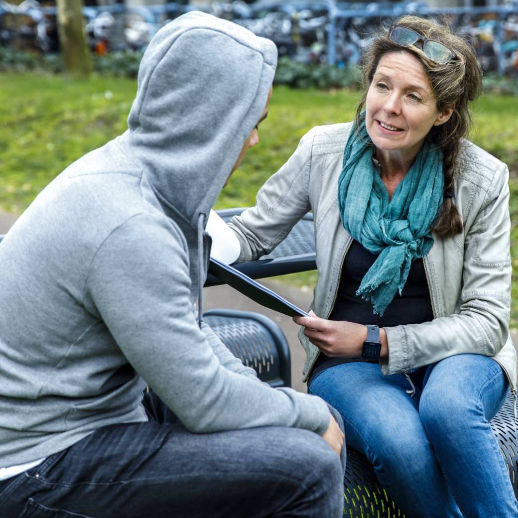 Een sociaal werker in gesprek met een man op een bankje.