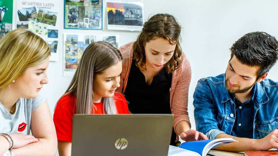 Docent aan de Lerarenopleiding Frans kijkt met haar drie studenten mee in het lesboek. 