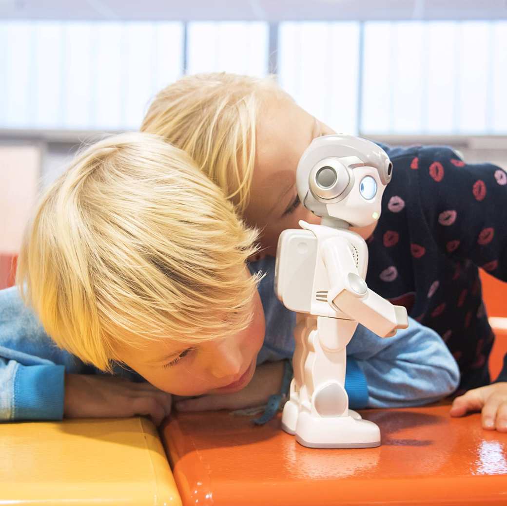 jongen en meisje met pen in mond verschuilen zich achter kleine zorgrobot tijdens iXbites event