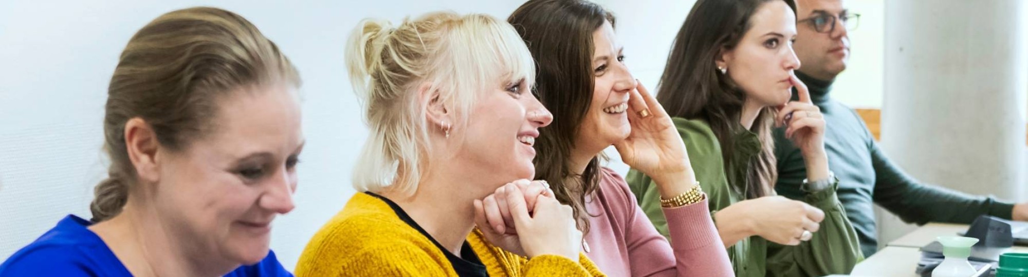 een rij van 5 masterstudenten zitten aan tafel met laptops