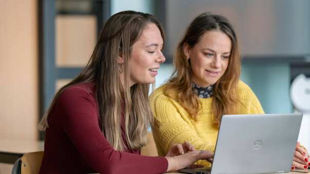 2 studenten kijken lachend samen naar een laptop.