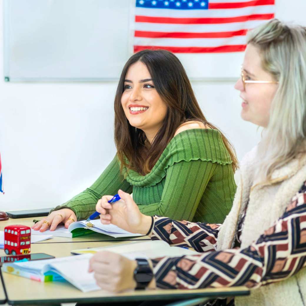 Twee studenten in een Engels lokaal. De foto is vanaf de zijkant gemaakt. Beide studenten lachen