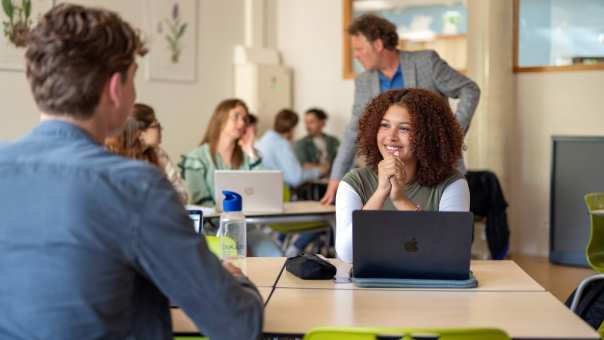 Meisje lacht en overlegt met een jongen, in de klas aan tafel. 