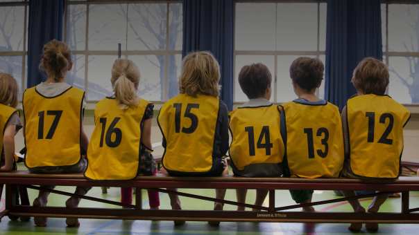 Kinderen in een gymzaal met hesjes aan op de rug gefotografeerd