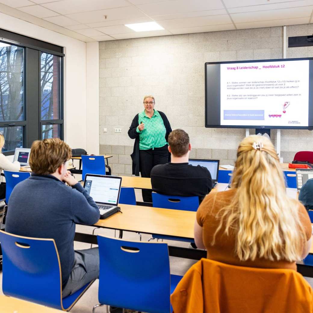 Docent geeft les aan deeltijd studenten die achter laptop zitten op de opleiding associate degree logistiek deeltijd