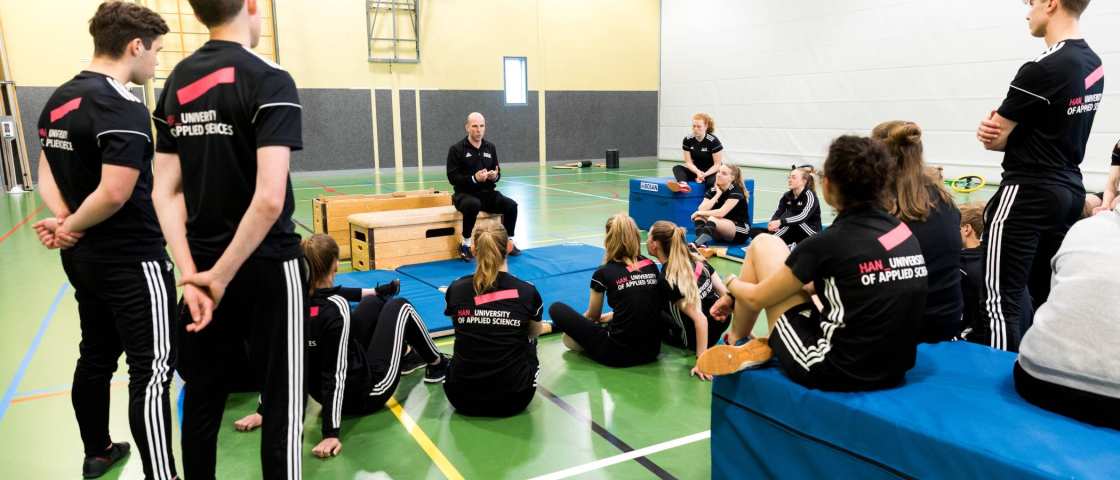 Pabo-ALO studenten zitten in de gymzaal rondom de docent die instructies geeft.