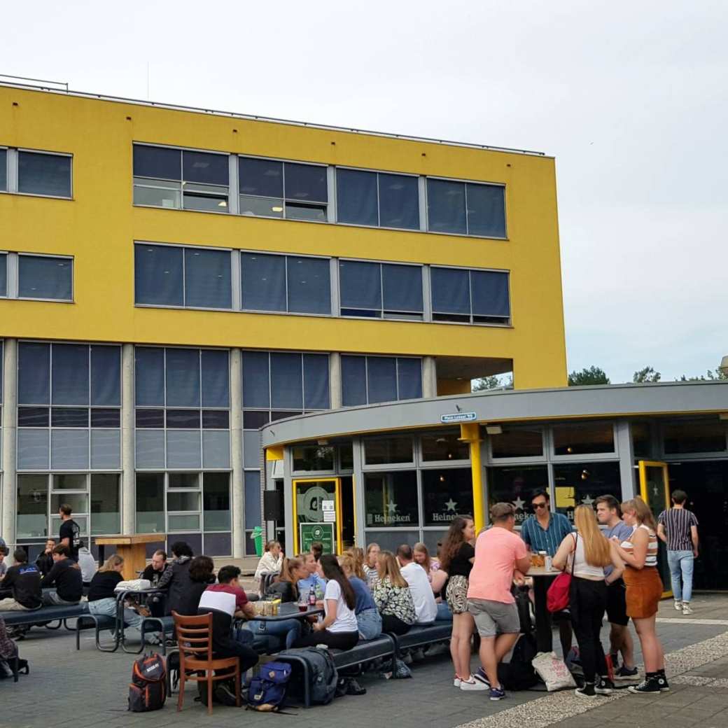 Studenten komen na de lessen samen bij Lokaal 99 om iets te drinken. Op de achtergrond het onderwijsgebouw van Engineering en Automotive.