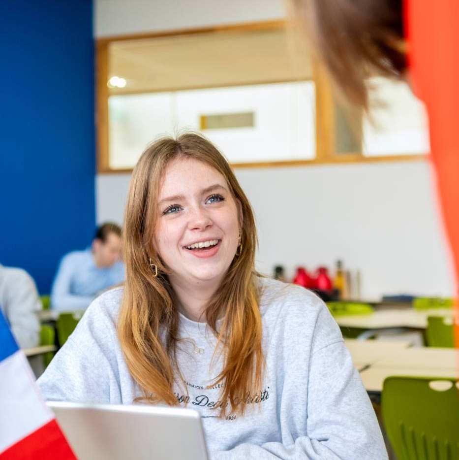 Drie studenten kijken lachend naar de ipad waar een medestudent iets aanwijst.