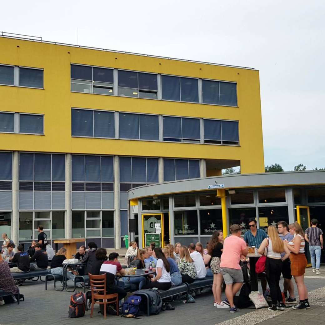 Studenten komen na de lessen samen bij Lokaal 99 om iets te drinken. Op de achtergrond het onderwijsgebouw van Engineering en Automotive.