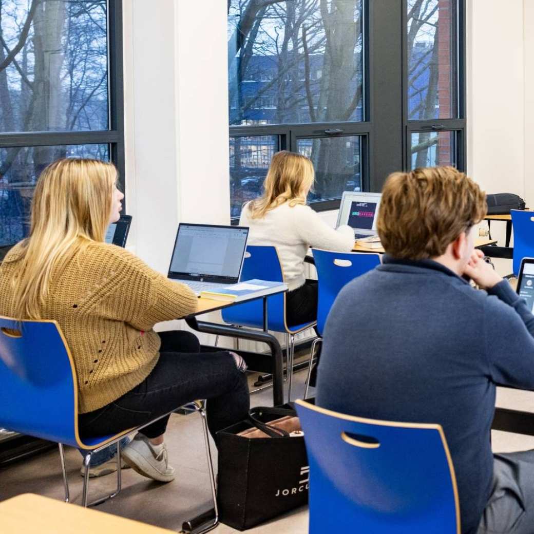 Studenten kijken bij elkaar op de laptop in een klaslokaal bij de opleiding bedrijfskunde duaal