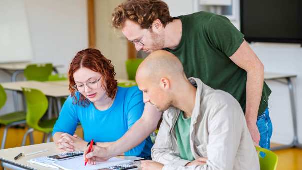 Leraar Wiskunde schrijft iets in het schrift van zijn twee studenten die met hem meekijken
