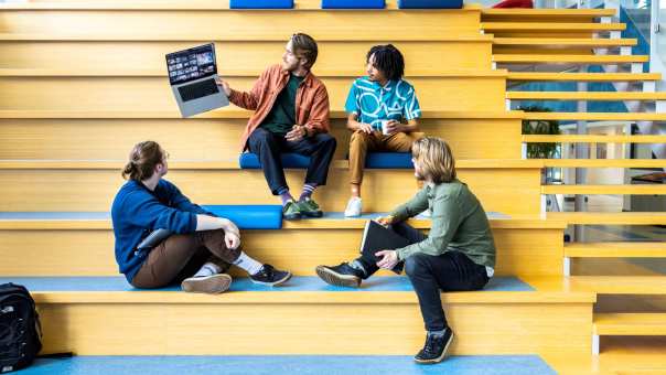 Docent CMD laat voorbeeld zien via zijn laptop aan studenten op de trap.