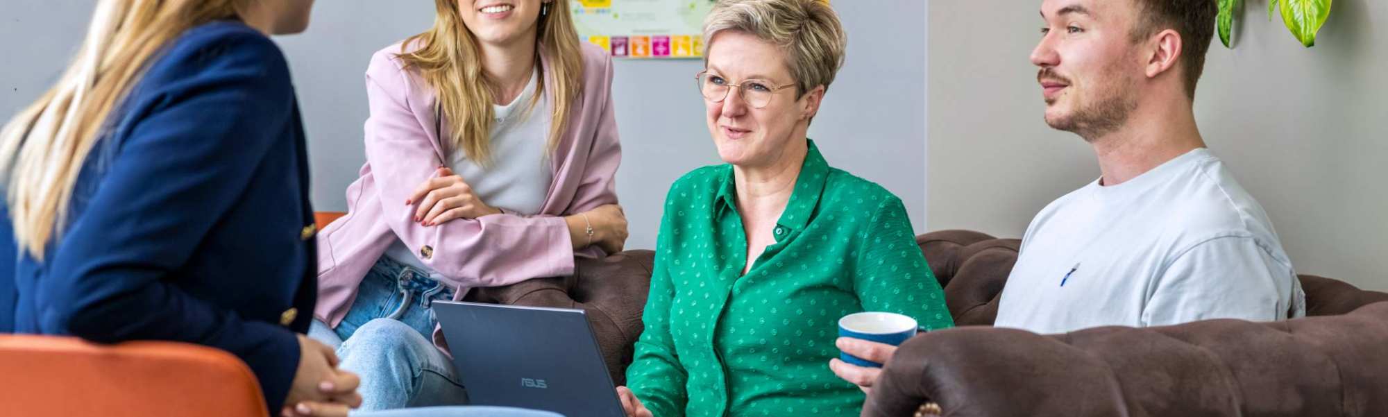 Vier studenten zitten met laptops bij elkaar en luisteren naar elkaar.