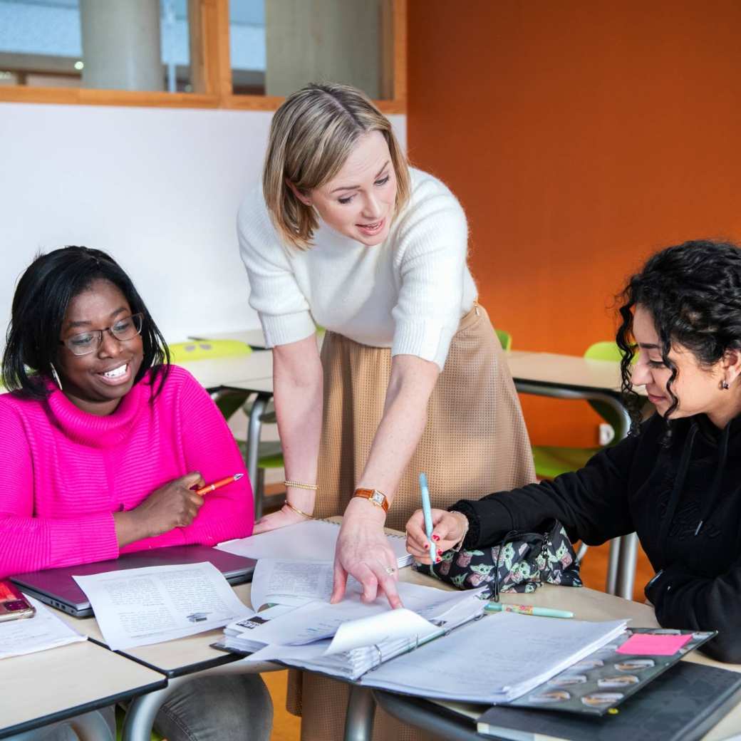 Twee masterstudentes aan tafel. De docente wijst iets in het schrift aan van de studente.