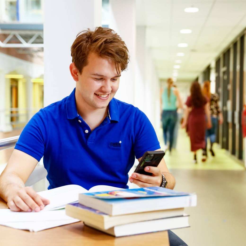 Communicatie en multimedia design student leest zijn telefoon in de gang van de HAN