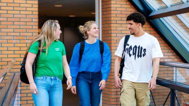 3 studenten lopen vrolijk over de brug met rugzak