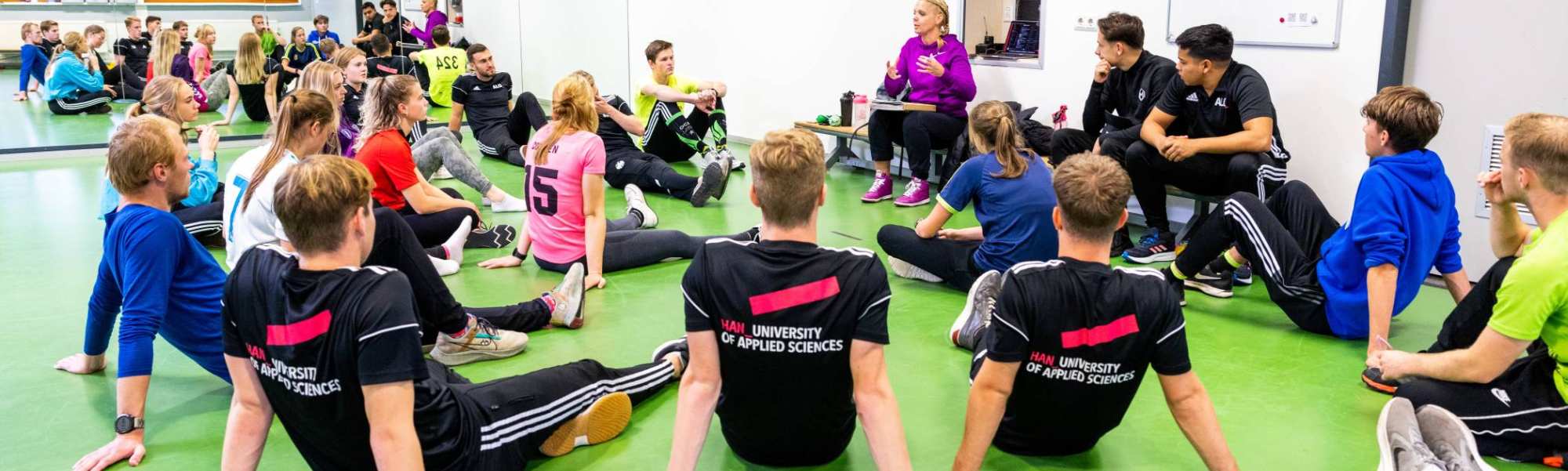 Studenten luisteren in de sportles naar docente.